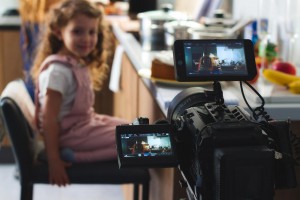 Video camera filming a movie scene with a young girl in the background